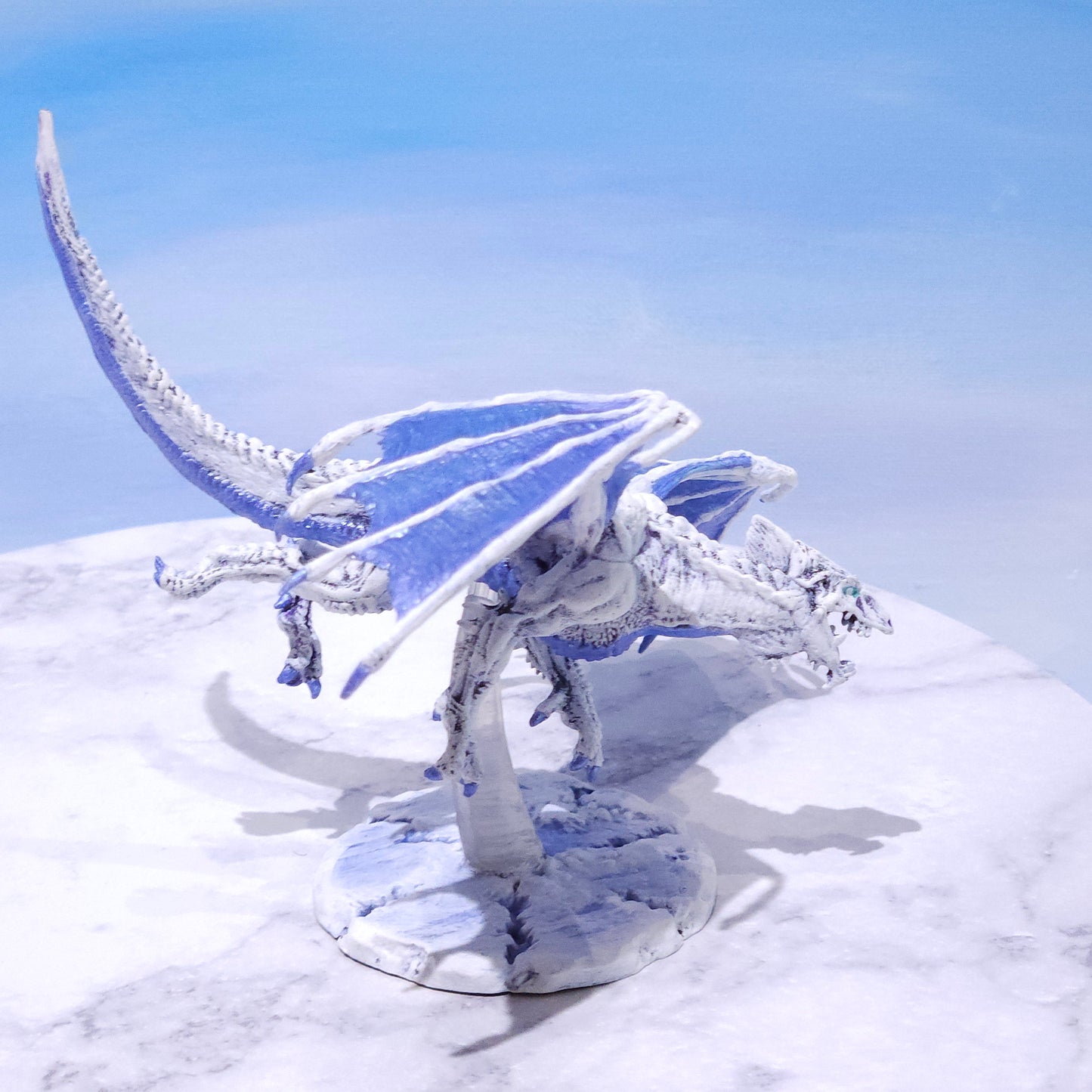 A white and light blue dragon figurine mounted on a round display base against a pale blue and white background.