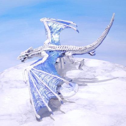 A white and light blue dragon figurine posed against a snowy white wall and pale blue sky background.
